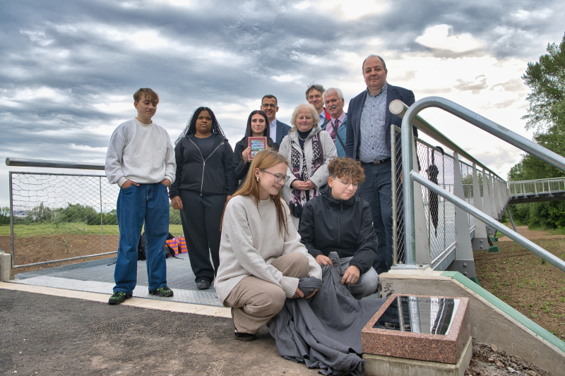 Schülergruppe, Familie Adler sowie Offizielle enthüllen den Namensstein der neuen Fernwärmebrücke.