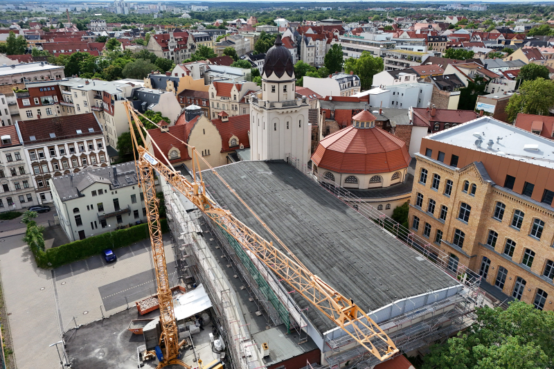 Luftaufnahme des historischen Stadtbades mit Kuppel und Turm, an dem ein großer Baukran Dacharbeiten ausführt.
