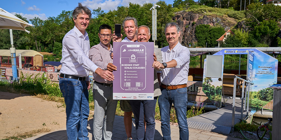 Matthias Lux und Peter Kolbert (beide Stadtwerke GmbH) halten gemeinsam, mit  Mark Lange vom Stadtmarketing Halle, Andreas Blümner vom Smart-City-Team Halle (Saale) und David Hauff von der Wassertouristik Saaletal, eine Werbetafel in der Hand.