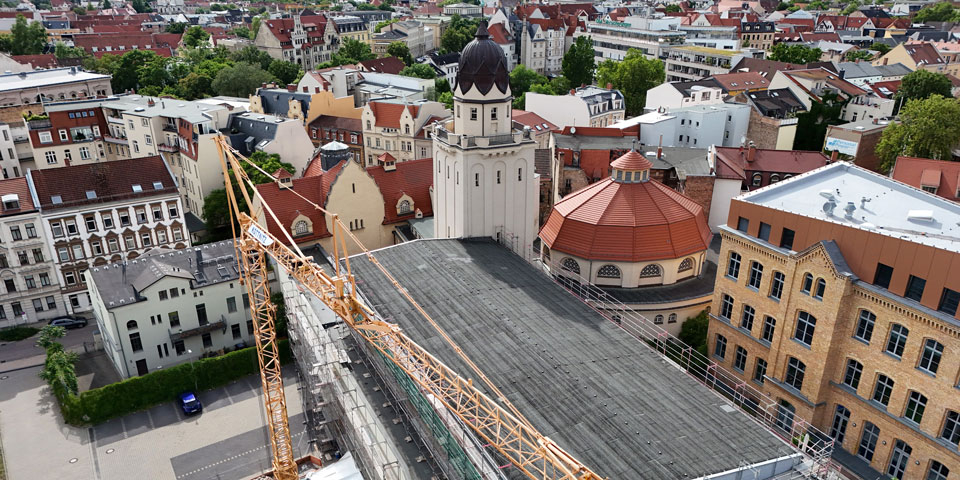 Luftaufnahme des historischen Stadtbades mit Kuppel und Turm, an dem ein großer Baukran Dacharbeiten ausführt.
