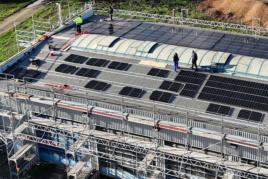 Mitarbeiter installieren PV Module auf dem Dach einer Werkstatthalle.