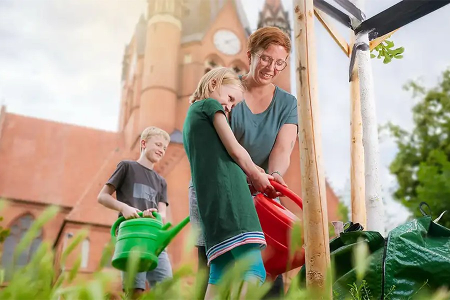 Mutter mit Kinder gießt einen Baum.