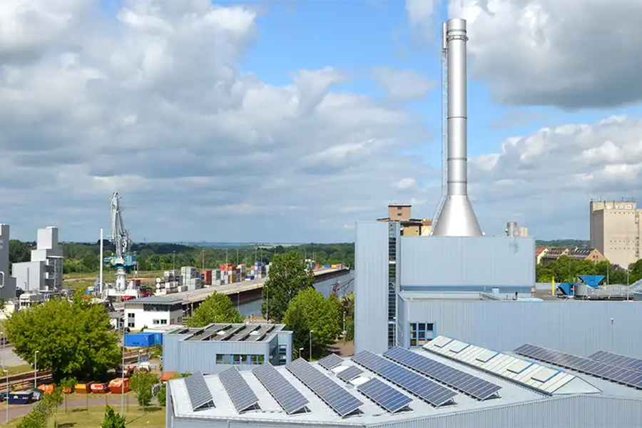 Kraftwerk mit Solaranlage auf dem Dach und hohem Schornstein am Kanal.