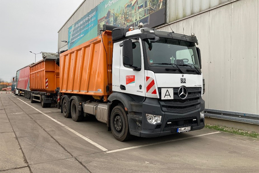 LKW mit orangenem Container und Anhänger.