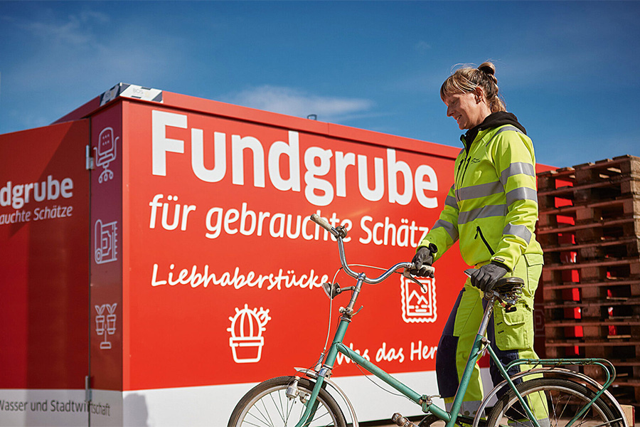 Mitarbeiterin mit einem Fahrrad vor dem Second Hand Container.