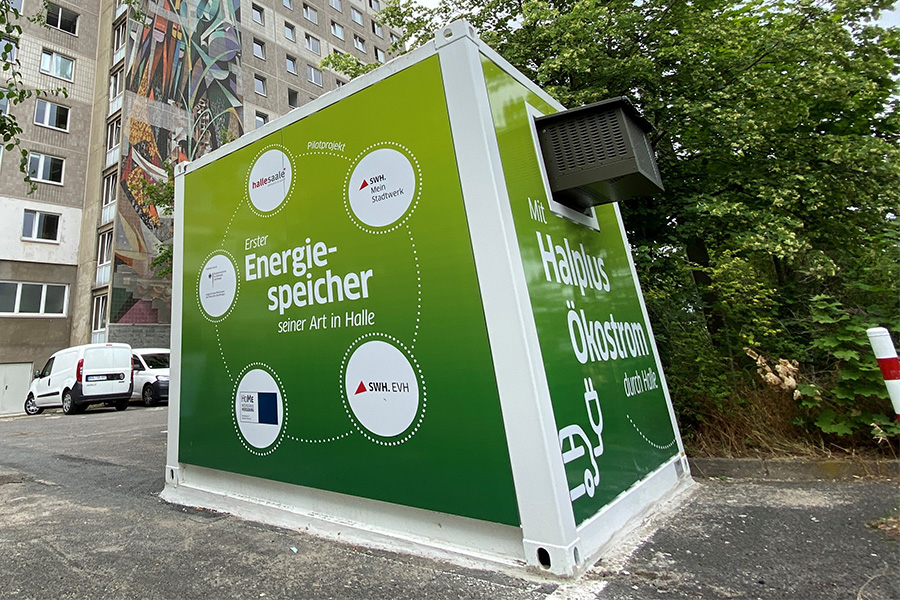 Grüner Energiespeicher-Container des Pilotprojekts von Stadtwerke Halle vor einem Wohngebäude.
