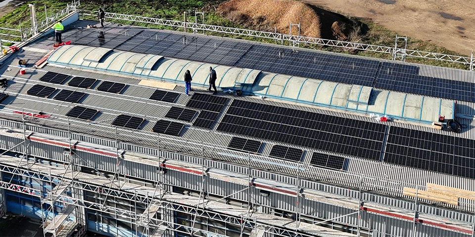 Mitarbeiter installieren PV Module auf dem Dach einer Werkstatthalle.