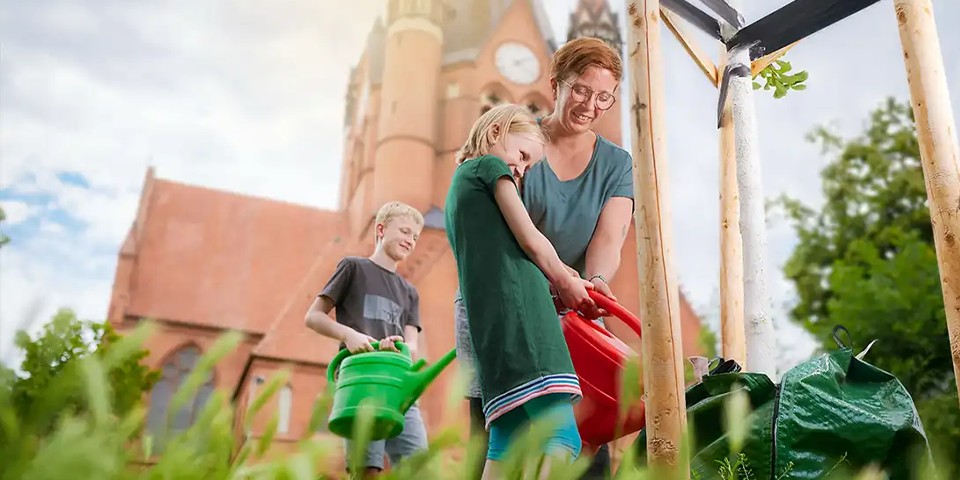 Mutter mit Kinder gießt einen Baum.