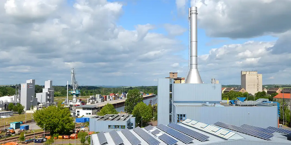 Kraftwerk mit Solaranlage auf dem Dach und hohem Schornstein am Kanal.