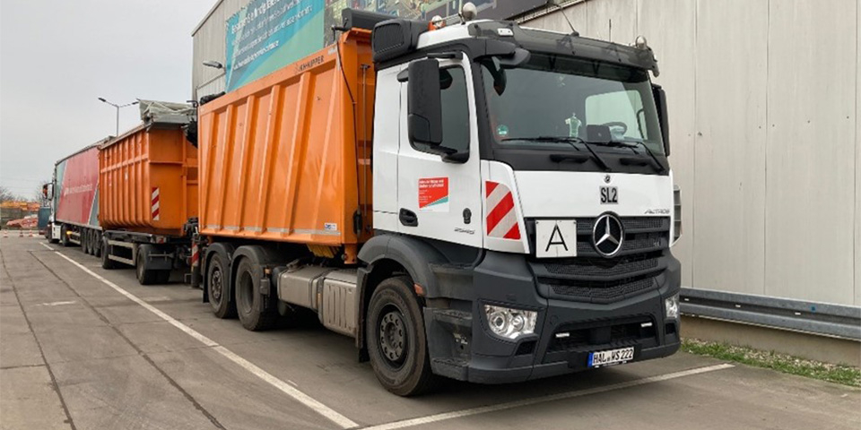 LKW mit orangenem Container und Anhänger.