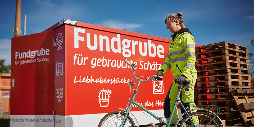 Mitarbeiterin mit einem Fahrrad vor dem Second Hand Container.