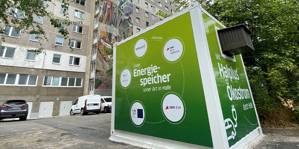 Grüner Energiespeicher-Container des Pilotprojekts von Stadtwerke Halle vor einem Wohngebäude.