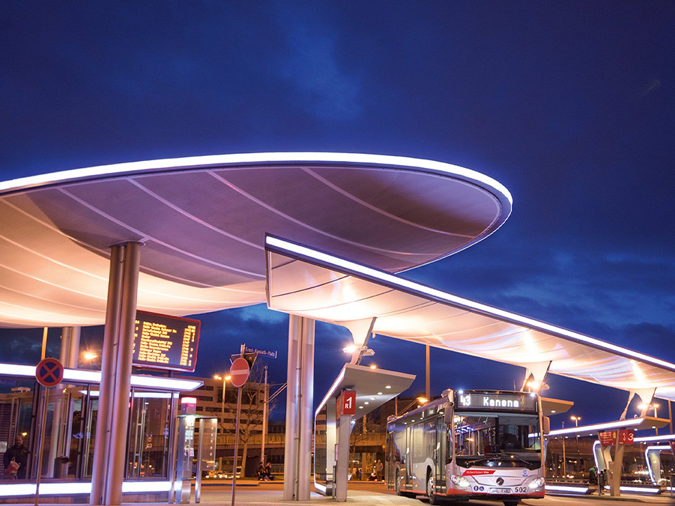 Beleuchteter Busbahnhof bei Nacht mit Bussen unter geschwungenen Überdachungen.