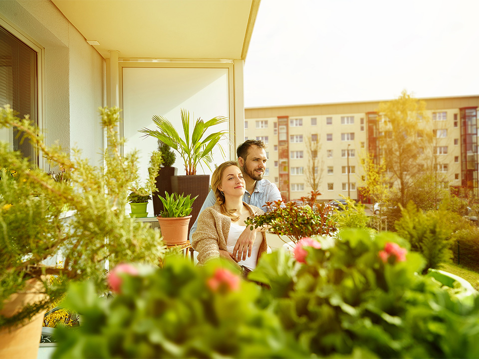 Frau und Mann sitzen auf begrüntem Balkon und blicken in die Ferne.